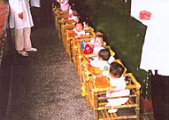Ten babies aligned in a row, in bamboo chairs.